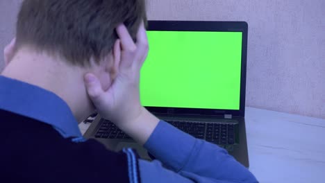 un tipo emocionalmente enojado por una conexión remota en una videoconferencia y golpea sus puños en una computadora portátil, pantalla verde