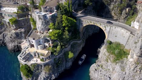 Puente-De-Arco-Fiordo-Di-Furore-En-La-Costa-Italiana-De-Almalfi-Con-Tráfico-De-Automóviles-Arriba-Y-Barco-Entrando-Abajo,-Tiro-De-Aproximación-De-Descenso-Aéreo