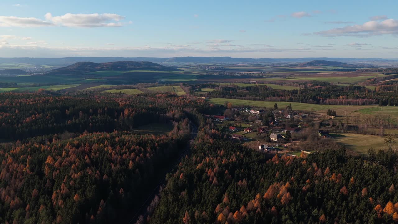 A small village in the middle of beautiful countryside, seen from the air at sunset. Trees and fields surrounding family homes. Drone view