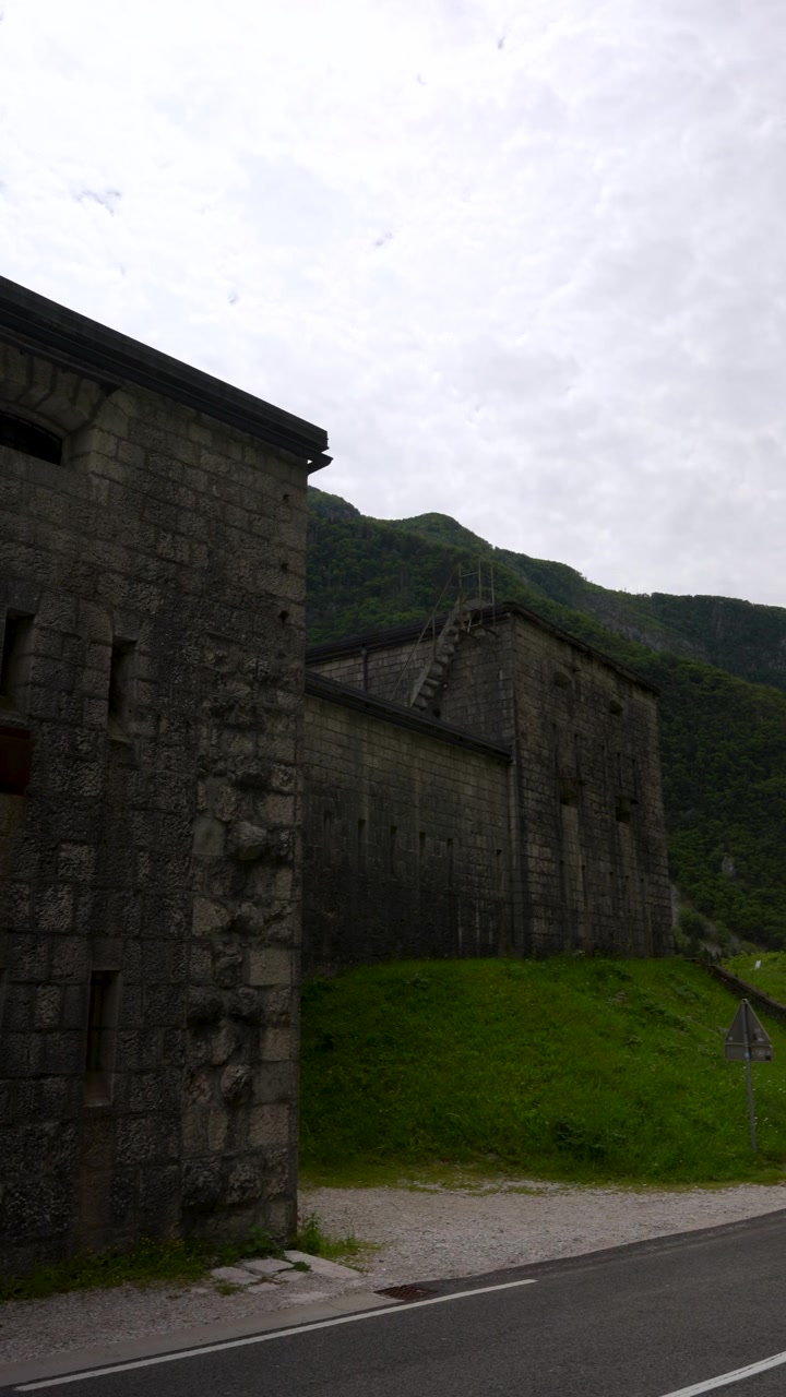 Eine filmische vertikale Schwenkfahrt der historischen Steinfestung Fort Kluze bei Bovec, Slowenien, die alte Militärarchitektur vor einer Bergkulisse zeigt