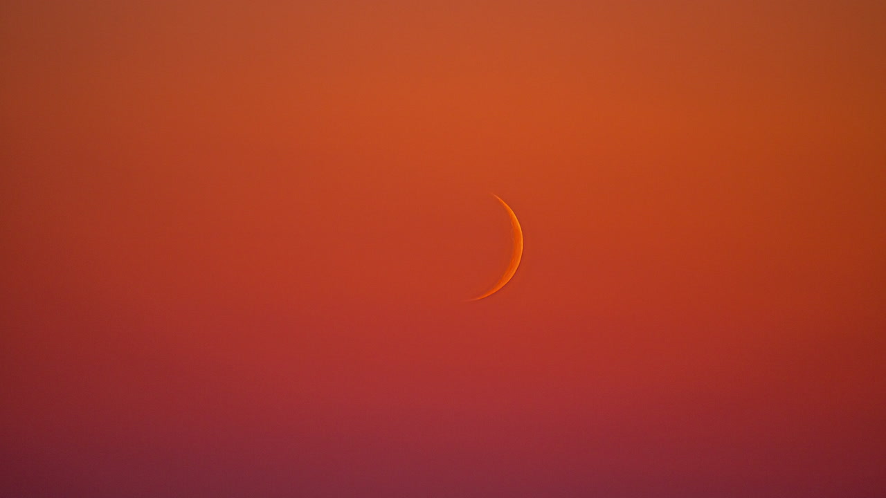 Wassende maansikkel bewegend in een vurige oranje zonsonderganglucht. Timelapse.