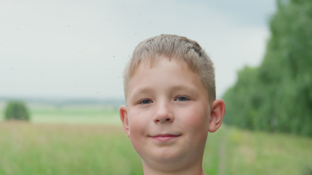 Ragazzo caucasico che tiene in mano una racchetta in un prato, ritratto delicato di un bambino timido che sorride leggermente con uno sfondo di campo verde, luce solare e brezza leggere, sguardo giocoso attraverso le corde della racchetta, atmosfera calda di vita rurale