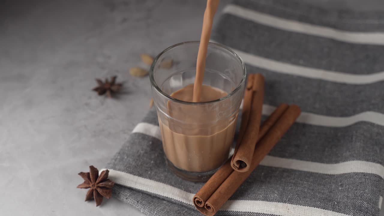 Chai indiano servito in tazze di vetro, preparato in un bollitore di metallo con masalas aromatici. Viene versato nel vetro.