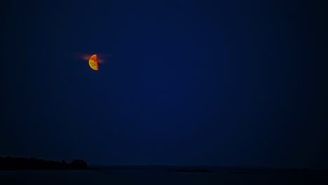 timelapse en una noche azul clara de media luna subiendo por el cielo nocturno sobre la costa del mar
