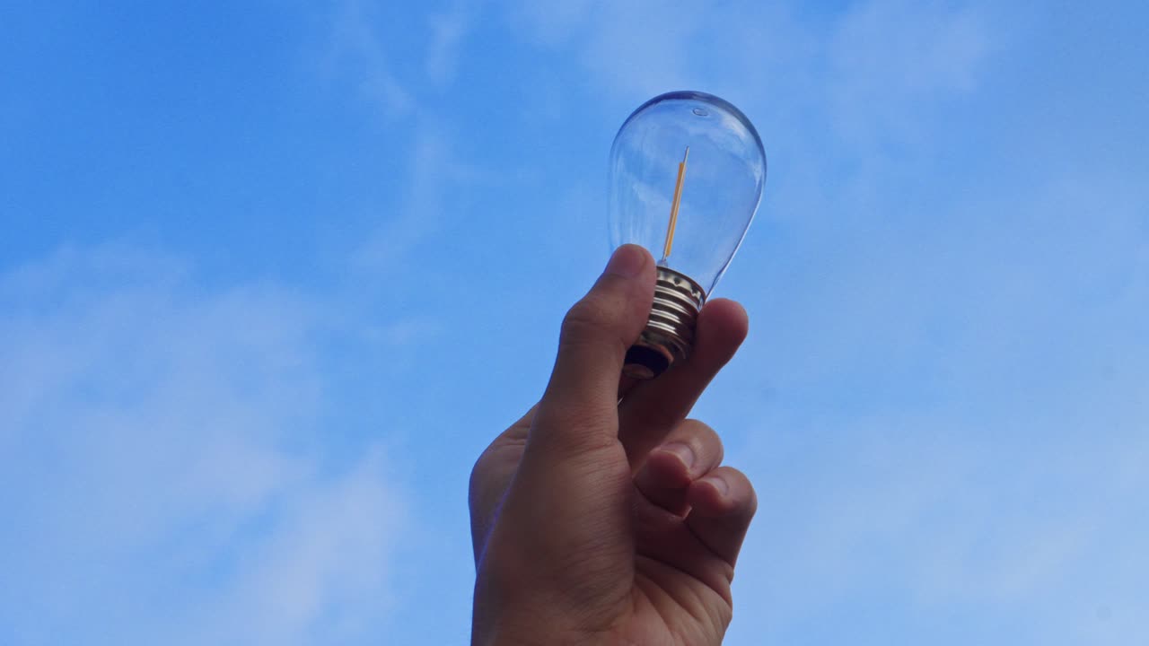 Hand holds single light bulb against bright blue sky