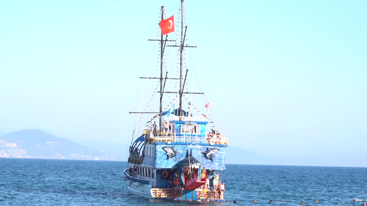 A pirate ship-themed cruise anchored on the sea, with tourists swimming in the water