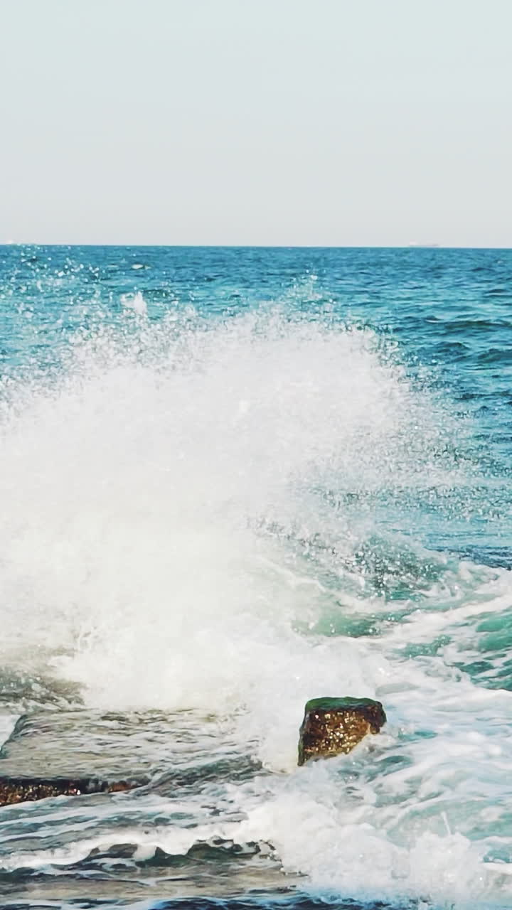 Sea waves are colliding with underwater reefs. Sea spray. Close-up. Water drops. Slow motion Vertical video