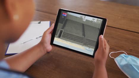 composite of woman sitting at table with face mask, watching athletics long jump event on tablet