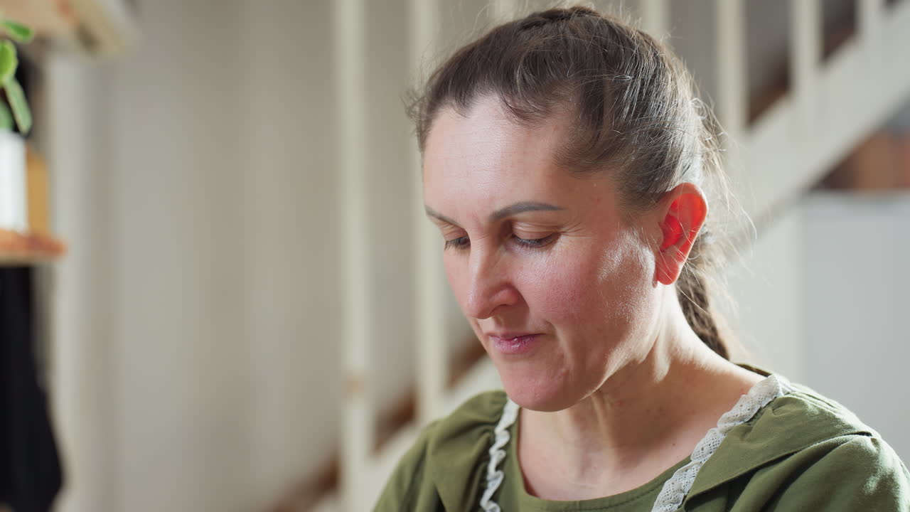 Middle-aged woman in green dress eats fresh berry with joyful expression in bright kitchen setting, savoring sweet taste with visible happiness
