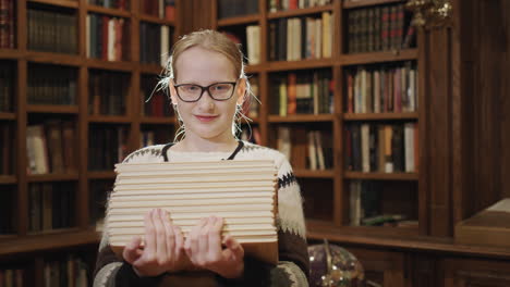 Portrait-of-a-11-year-old-girl-with-a-textbook,-stands-against-the-background-of-bookshelves-in-the-library
