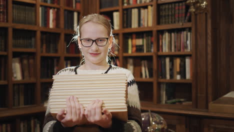 retrato de una niña de 11 años con un libro de texto, de pie contra el fondo de las estanterías de la biblioteca