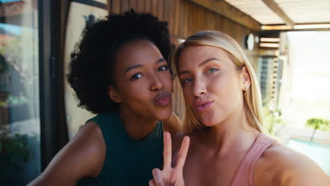 una foto de amigas sonrientes al aire libre en casa posando para una selfie en el teléfono móvil juntas