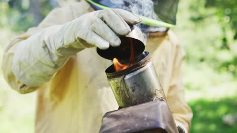 caucasian male beekeeper in protective clothing preparing smoker