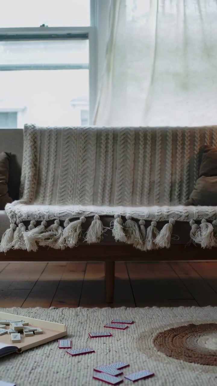 Vertical video: Framing bench with chunky cream throw at window, curtain swaying from breeze