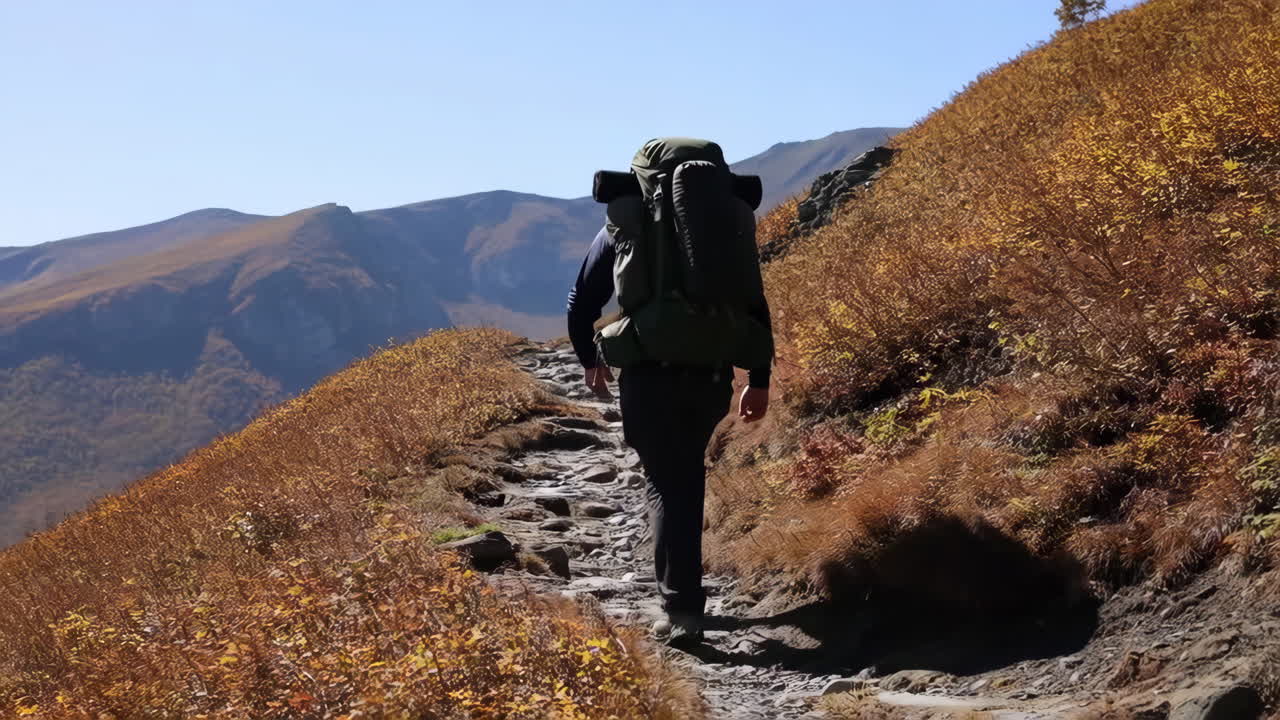 Backpacker Hikes Uphill on a Rocky Mountain Trail in Autumn
