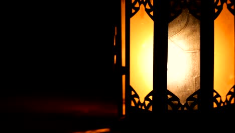 view of a classic arabian lantern, with an orange light because of the burning flame. everything is dark around the lantern.