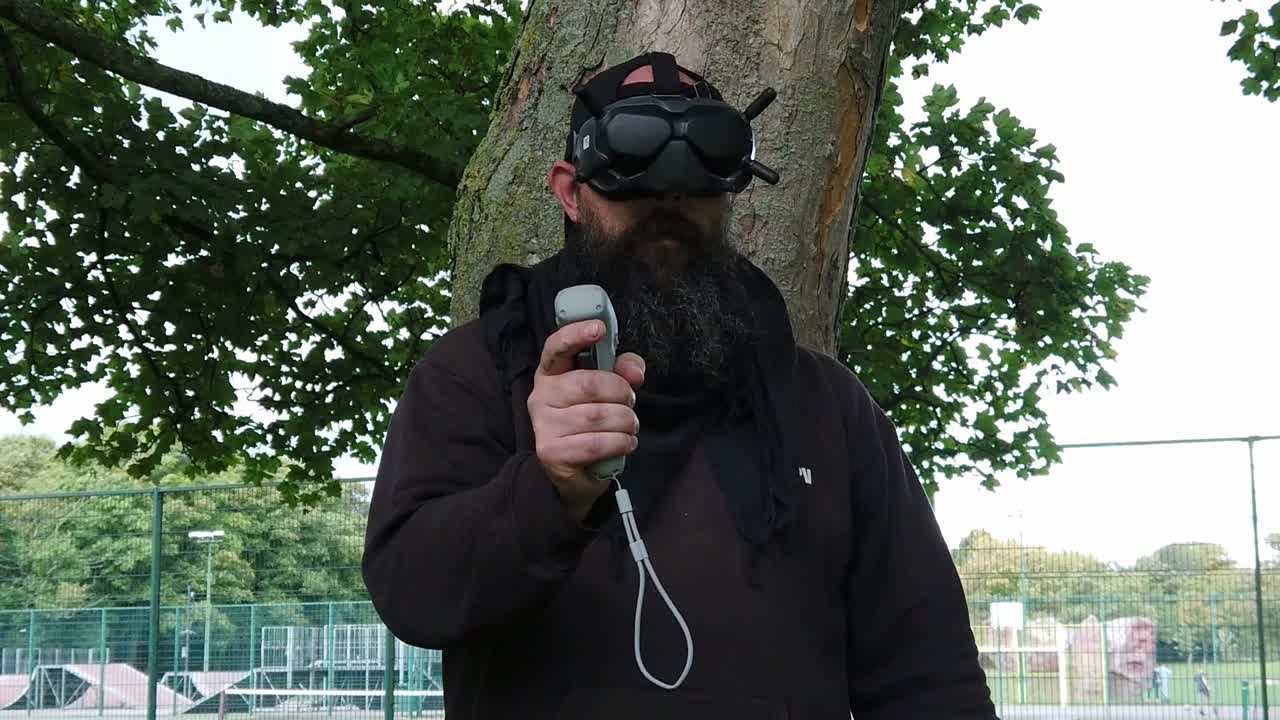 hombre barbudo con gafas fpv digitales que controlan drones en el parque con joystick de movimiento