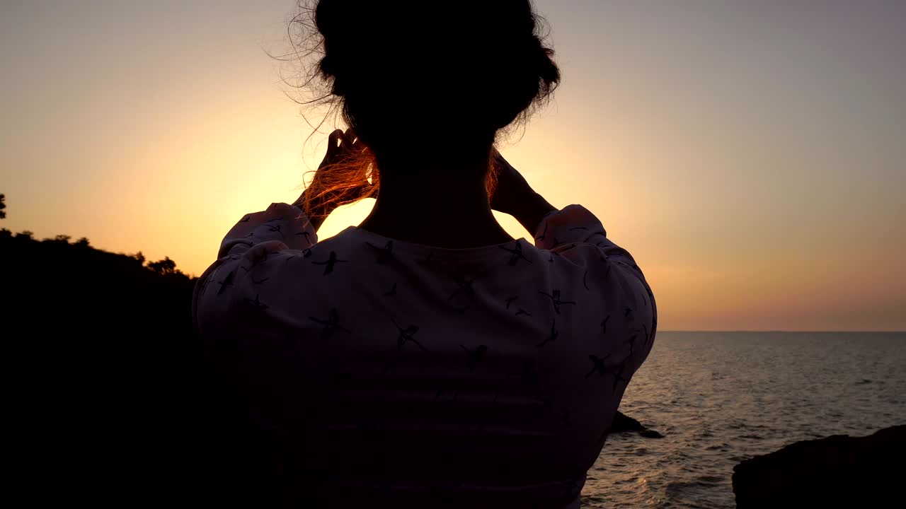 晴れたドレスを着た可愛い白人の茶色の女の子が日の出時に海上の崖を撮影するためにスマートフォンを使用しています