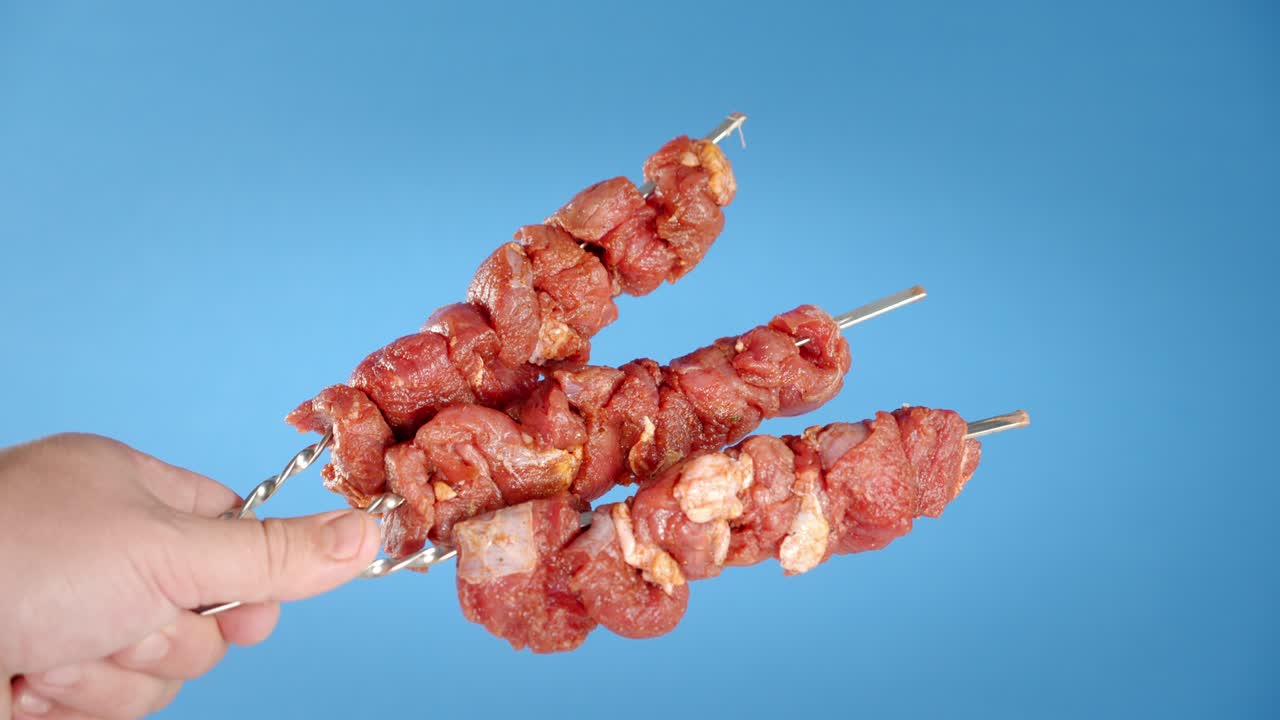 un pinzón con kebab de cerdo crudo sostiene la mano de un hombre.