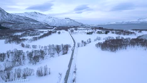 Aerial-forward-shot-of-car-driving-on-road-on-Andoya-Island-during-beautiful-snowy-winter-day-in-Norway