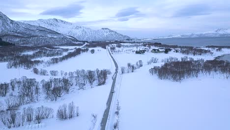 fotografía aérea de un coche conduciendo en la carretera de la isla de andoya durante un hermoso día de invierno nevado en noruega