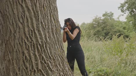 mujer detrás de un árbol apuntando un rifle de francotirador y disparando