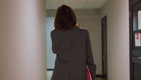 businesswoman walking down office corridor, carrying red folder, professional environment, confident professional in gray suit, work setting, modern office, corporate workplace, career focus