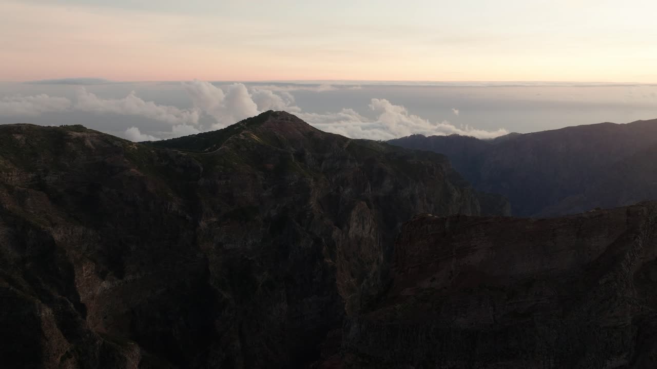 Massive rugged cliffs at Pico do Arieiro rise above the cloud line under soft pastel light at dawn in Madeira, Portugal.