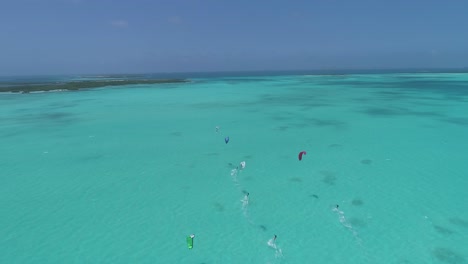 Group-of-people-kitersurfers-sail-on-tuquoise-sea-water,-drone-tracking-shot