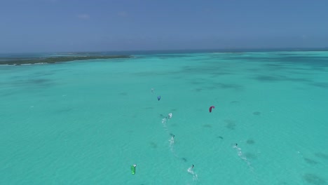 Gruppe-Von-Menschen-Kitersurfer-Segeln-Auf-Türkisblauem-Meerwasser,-Drohnenkamerafahrt