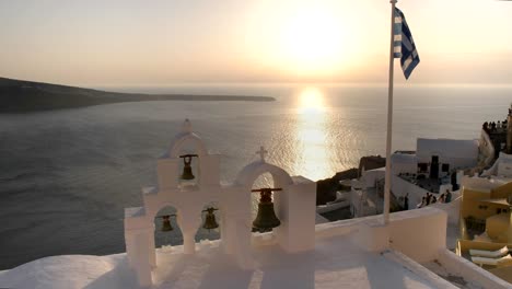 greek flag and four bells at sunset in oia, santorini