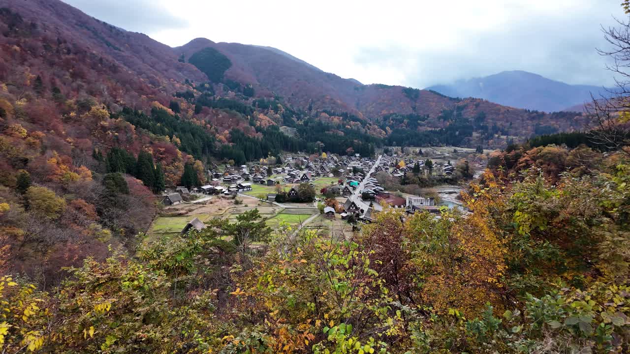 Shirakawa-go village from a viewpoint with beautiful autumn foliage and scenic mountains. pan left