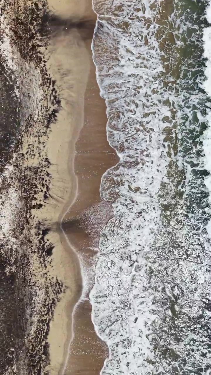 Le onde si frangono su una spiaggia sabbiosa mentre la marea rifluisce nell'oceano sotto un sole splendente nel pomeriggio.