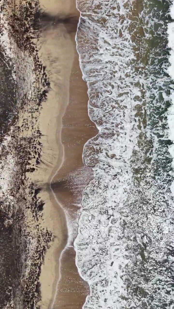 Le onde si frangono su una spiaggia sabbiosa mentre la marea rifluisce nell'oceano sotto un sole splendente nel pomeriggio.