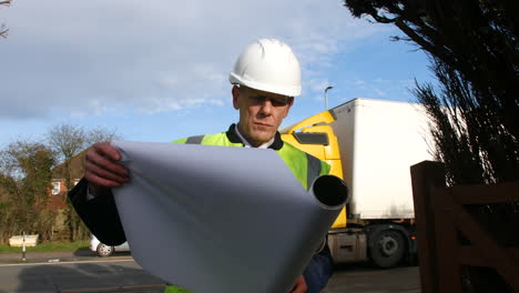 An-architect-unrolling-plans-of-a-building-on-a-construction-site-in-a-residential-street-with-traffic-on-the-road-in-the-background