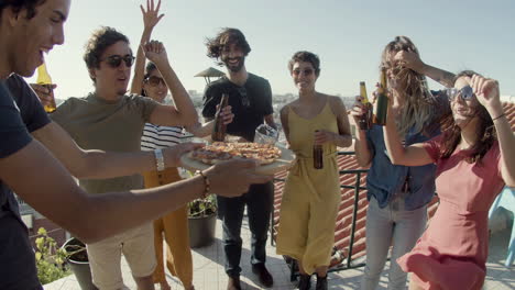 happy man carrying pizza to friends during a rooftop party