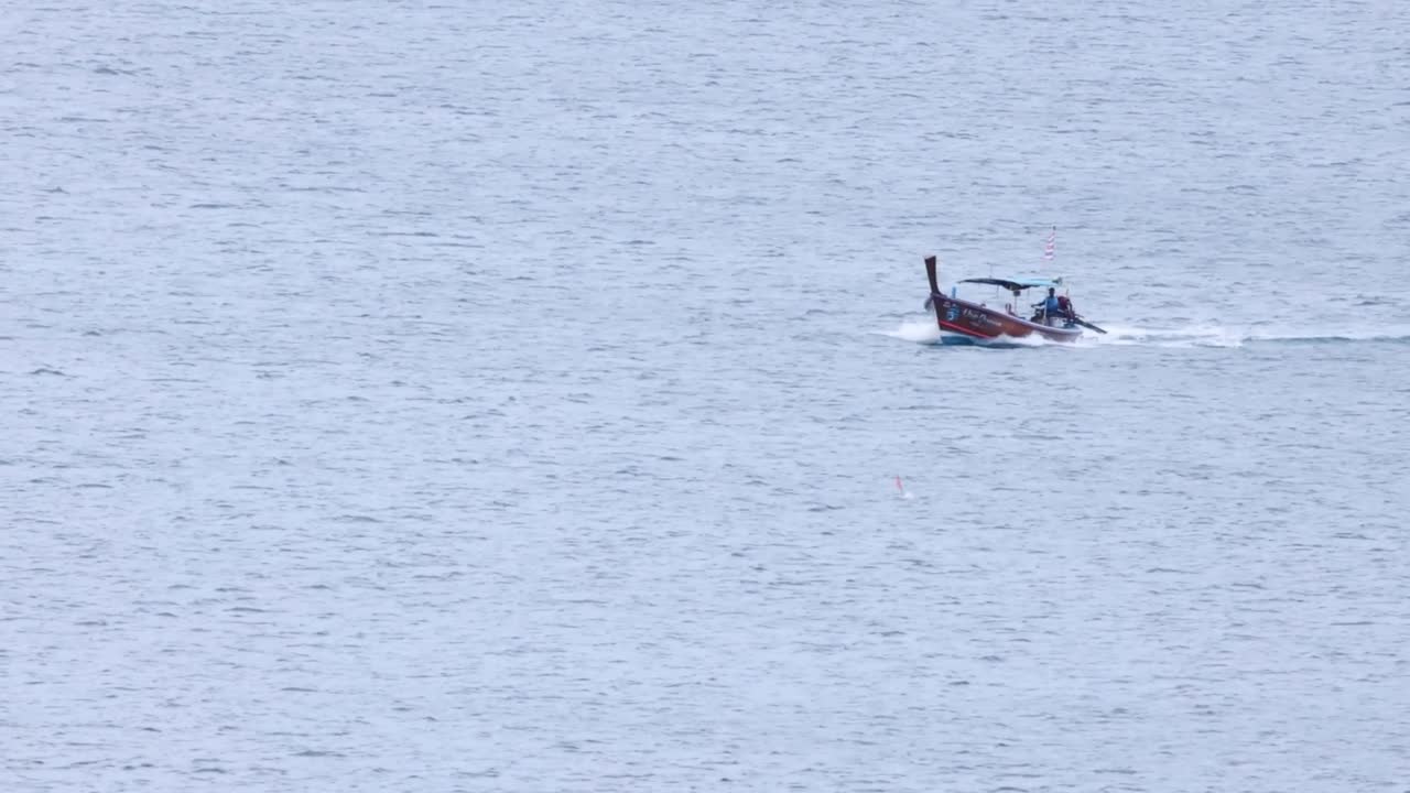 A traditional longtail boat moves steadily across the expansive ocean, leaving a gentle wake behind.