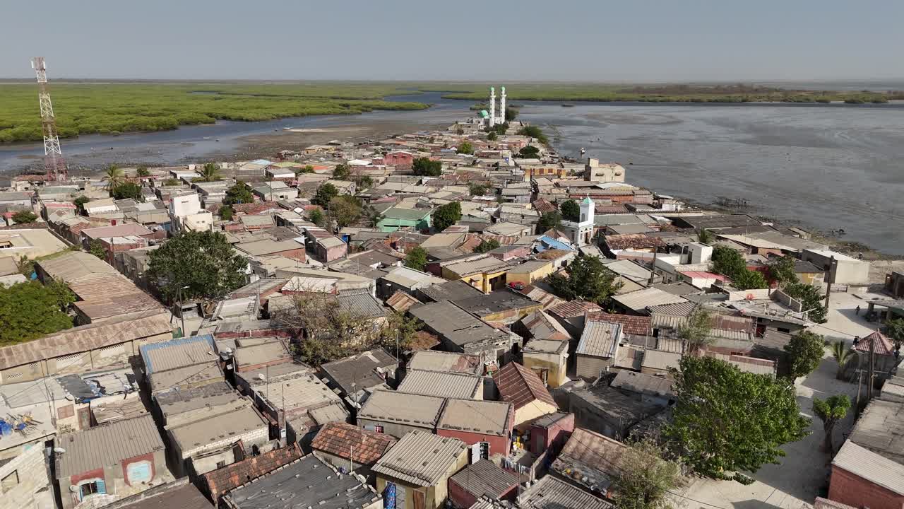 Drone aerial view of Joal Fadiouth village in Senegal, with houses clustered along the shoreline, showing cultural heritage and African lifestyle