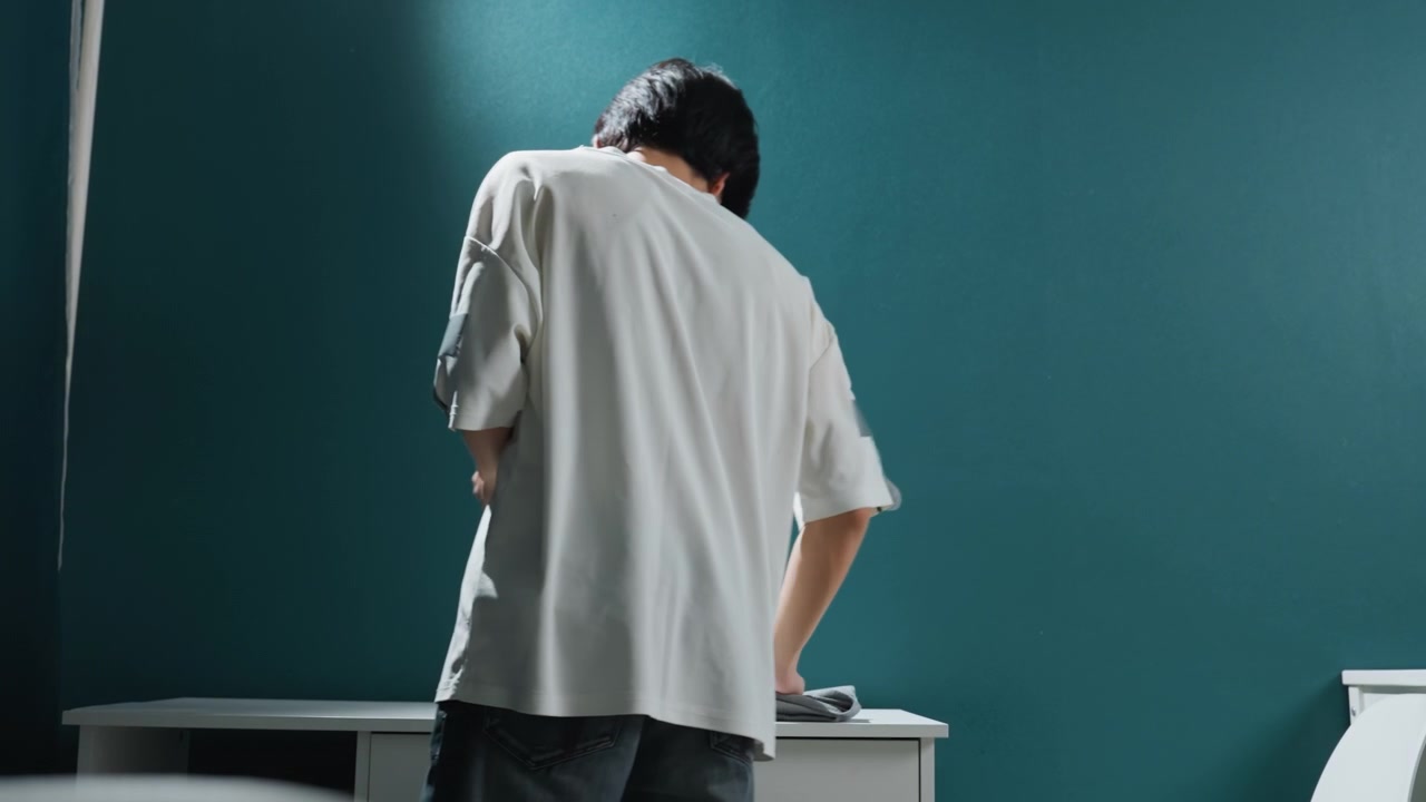 Uomo asiatico sistema un piccolo monolocale. Persona che allestisce metodicamente lo spazio di lavoro all'interno di un piccolo appartamento. Maschio asiatico che sistema attentamente mobili e oggetti all'interno di un monolocale minimalista.