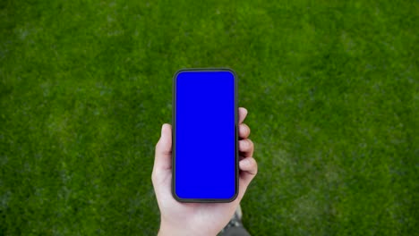 person walking and use green screen chroma key phone point of view. caucasian man hold in hand smartphone mock-up and watching video content, browsing internet news. go on grass mobile phone close-up