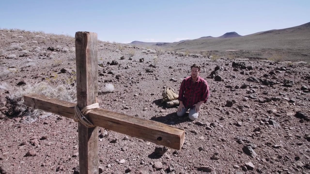 Uomo Inginocchiato in un Paesaggio Desertico Arido con Croce di Legno