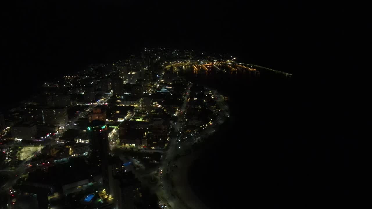Luminous urban landscape of Punta del este Uruguay spreading along coastal shoreline, revealing sparkling metropolitan scenery beneath darkening sky with expansive nighttime panorama