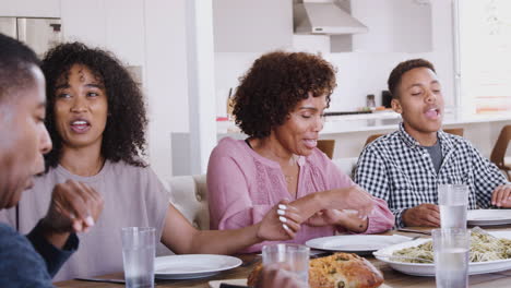 close up of a black family sitting at the dinner table saying grace then serving food