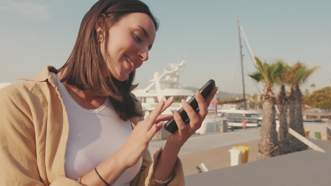 Ung kvinne smiler mens hun bruker smarttelefon i marina