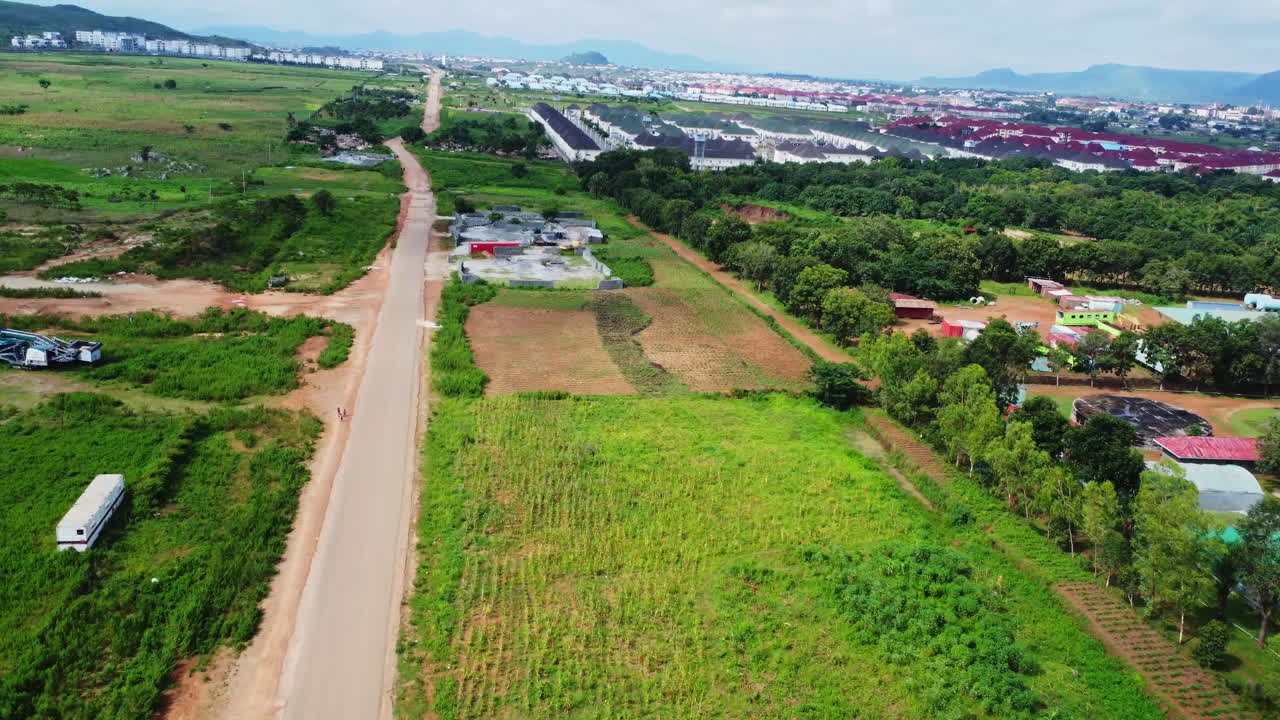 Drone flying over a long road with farms and agricultural industry in a beautiful countryside in rural Nigeria, Africa on a sunny day. Beautiful housing units and cabins can be seen