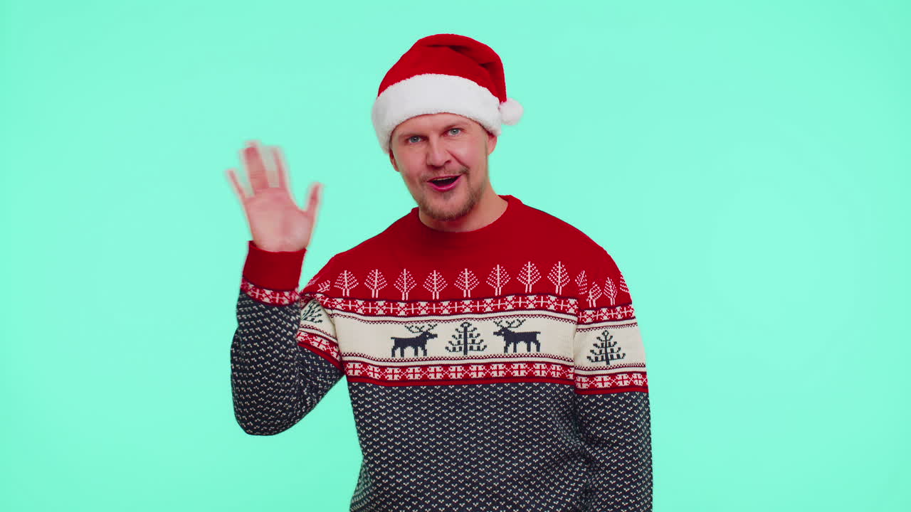 Man in red Christmas sweater waves hand palm in hello gesture welcomes someone to celebrate New Year