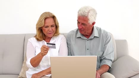 retired smiling couple using their laptop to shop online on the couch