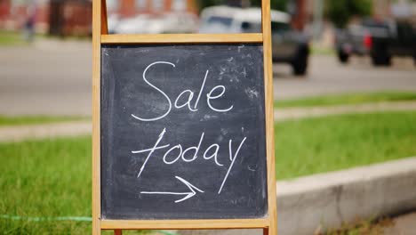 sale today chalkboard and wood a-frame sign outside next to green grass and road with cars driving by in the middle of the day, centered in frame