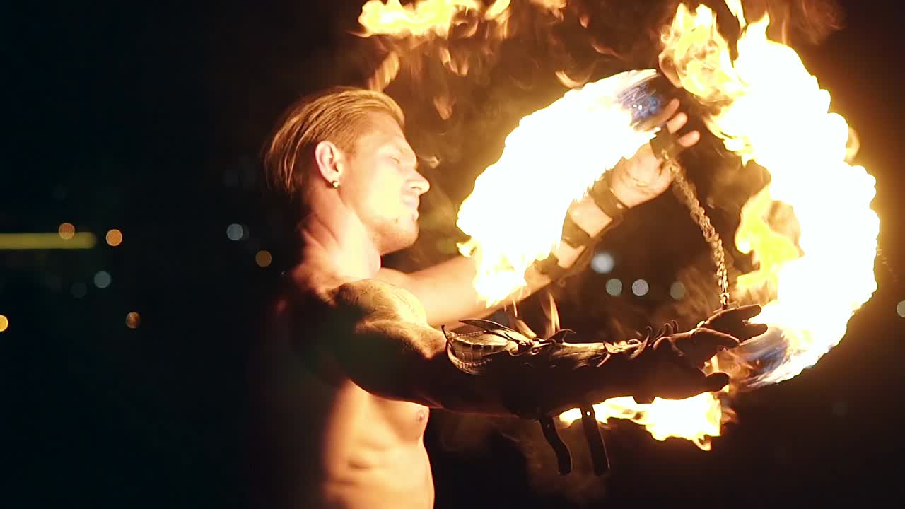 Young blond male spins two burning pois tied together Slow motion shot Close-up