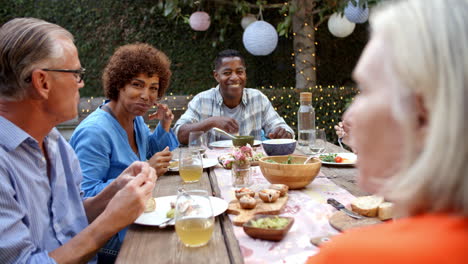 Group-Of-Mature-Friends-Enjoying-Outdoor-Meal-In-Backyard